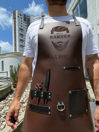 Barber wearing a dark brown apron engraved Best Barber Mauricio, with scissors in the tool loops