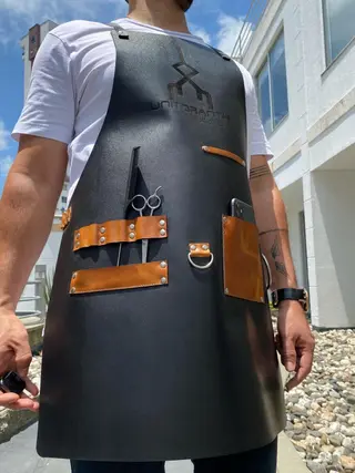 Black barber apron with a tan pocket and tool loops, worn
