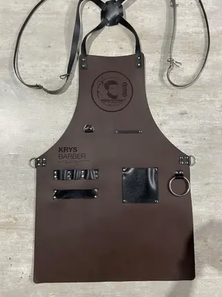 Dark brown barber apron with a round engraved logo and a black pocket