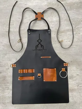 Black barber apron with a tan pocket and an engraved logo