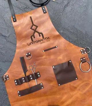 Tan barber apron with dark brown pockets and an engraved logo