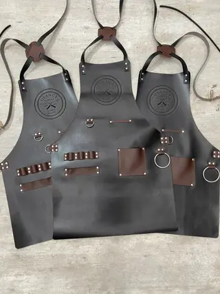 Three barber aprons with engraved logos, side by side