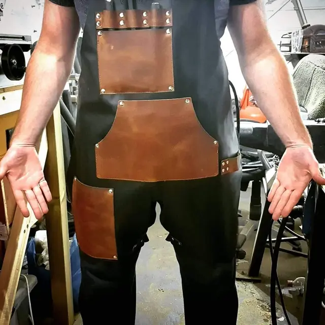 A craftsman in a workshop wearing a black and tan split-leg leather apron